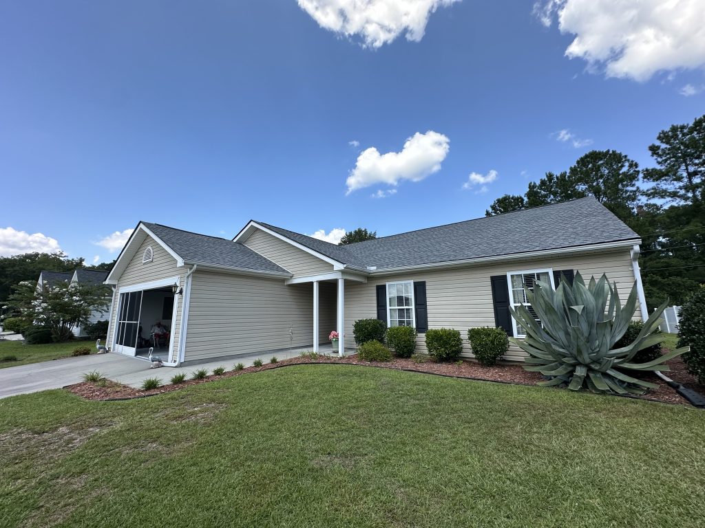 IMG_6794 Tan single-story home with new dark gray shingle roof under a partly cloudy sky in Myrtle Beach, SC