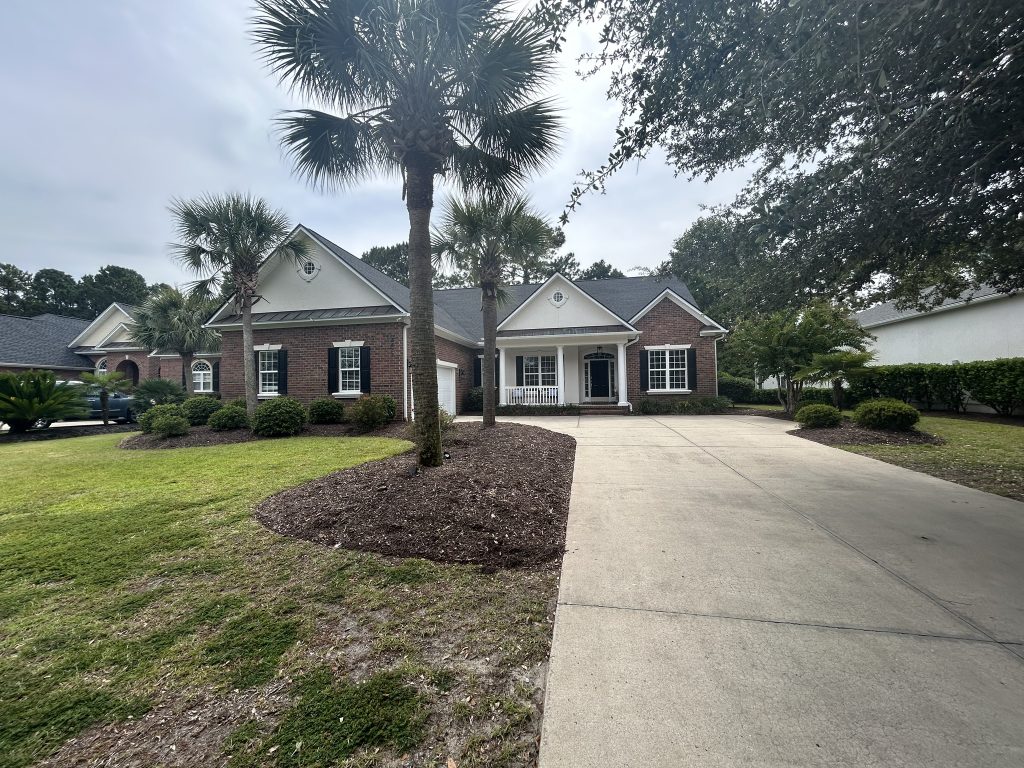 item_19c1c5ea-3fa1-46cc-8c42-6a33a0a91234 Two-story home with dark shingle roof viewed from a palm-tree-lined driveway in Myrtle Beach, SC