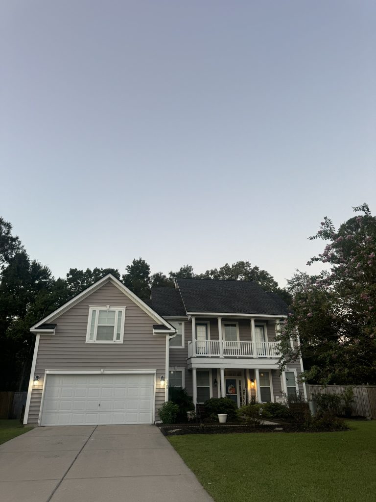 Two-story tan home with a covered upstairs porch and new dark shingle roof photographed at dusk in Charleston, SC