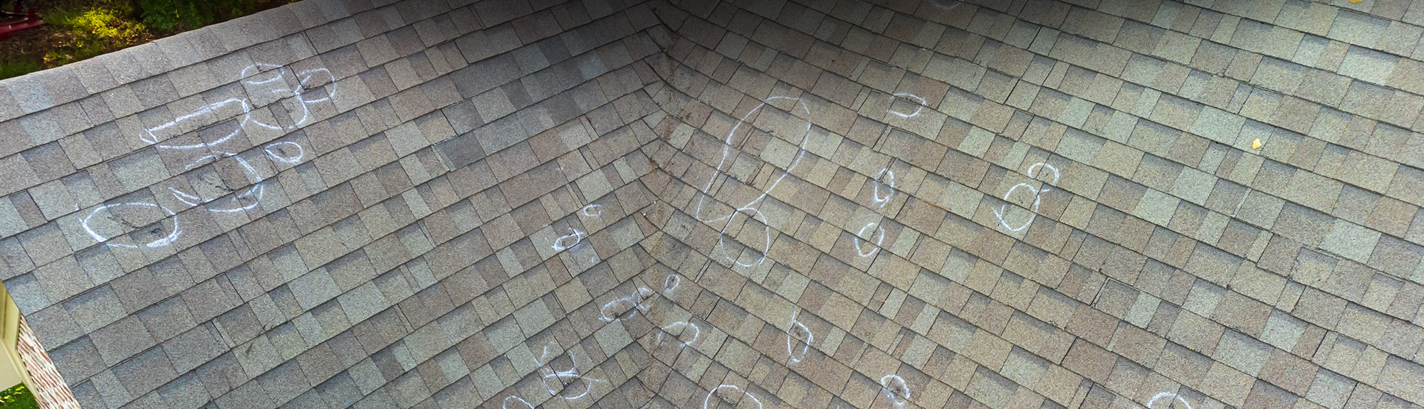 Asphalt shingle roof with hail impact points circled in chalk during an inspection