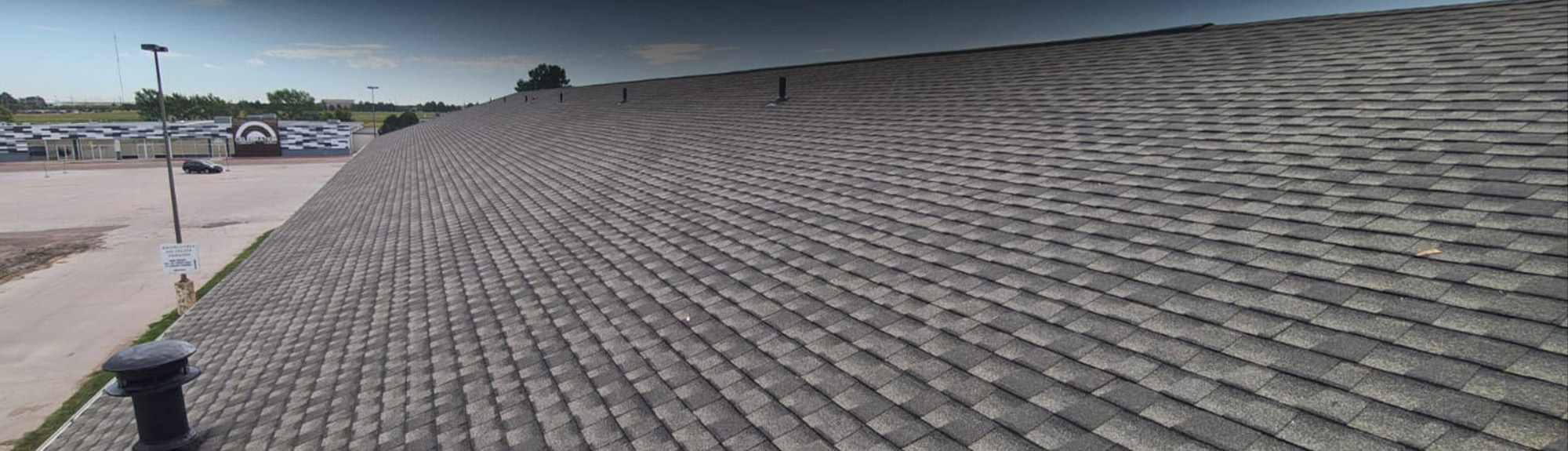 Wide-angle view of a commercial building's shingle roof with vent stacks, an example of commercial roofing Wichita businesses trust us with