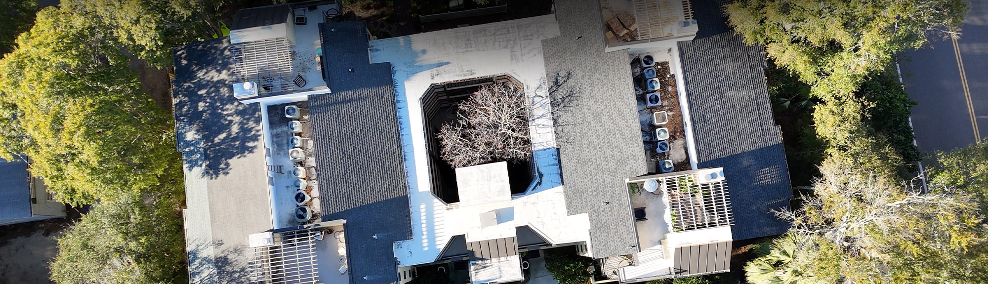 Aerial drone view of a flat and low-slope commercial roof surrounded by trees, an example of commercial roofing Springfield MO buildings need